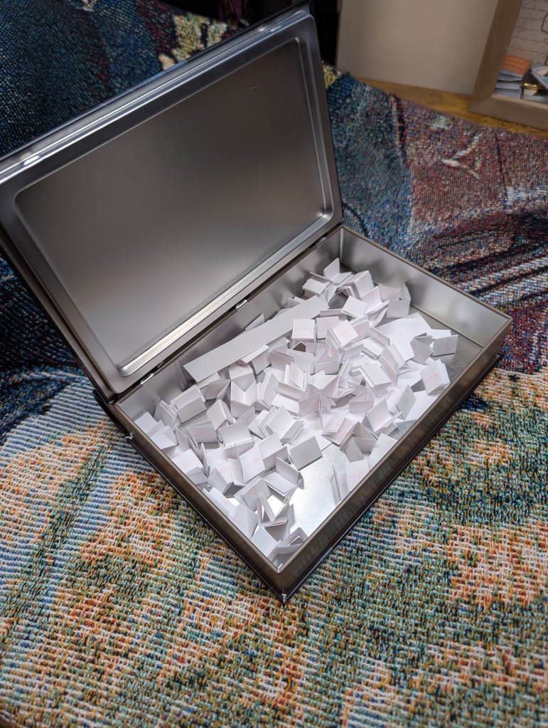 Image of the open tin with a plethora of folded up pieces of paper inside